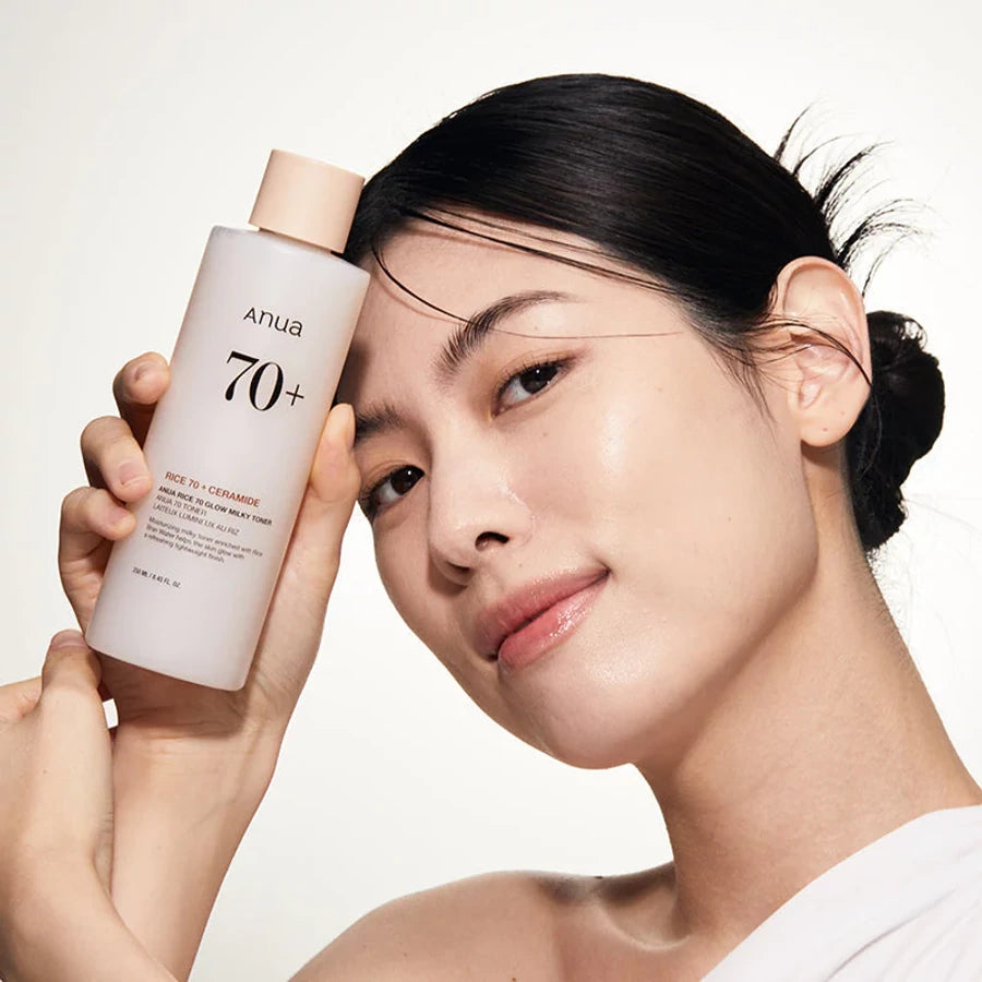 Décris l’image en français : ANUA Rice 70 + Ceramide Glow Milky Toner 250ml d’ANUA, sur une femme au visage, fond clair.