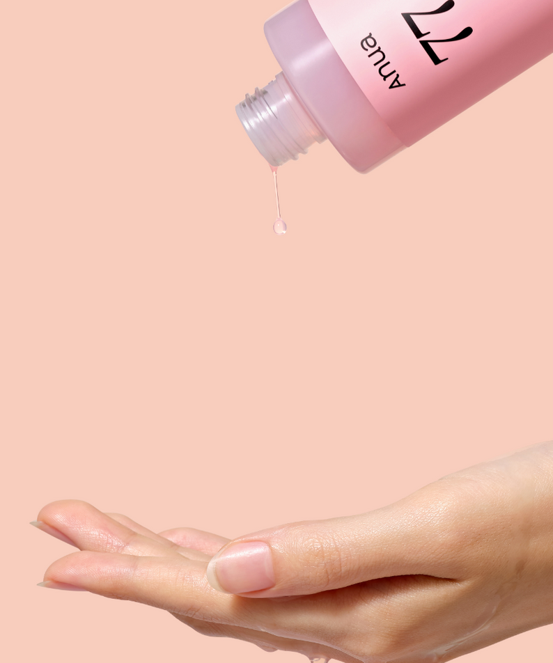 ANUA Peach 77 + Niacin Essence Toner 250ml, flacon sur peau, main applique le sérum, fond rose, marque ANUA