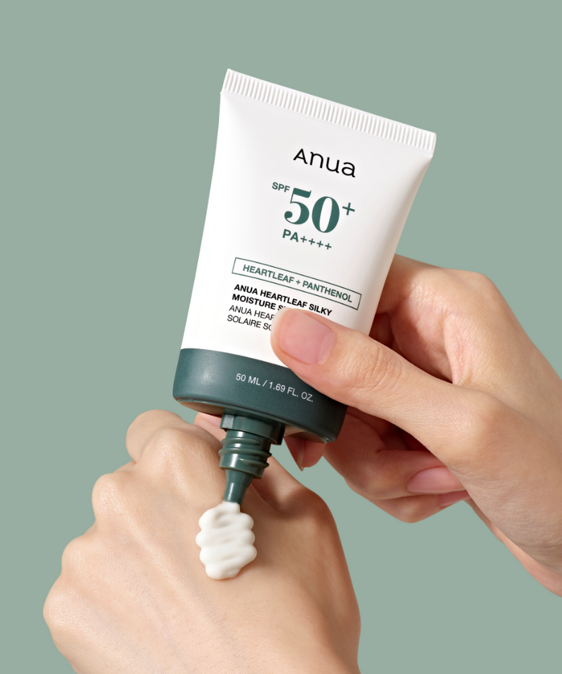 Main tenant ANUA Heartleaf Silky Moisture Sun Cream 50ml, tube crème solaire Anua, arrière-plan vert uni.