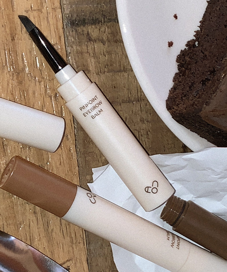 AOU Pinpoint Eyebrow Balm de la marque AOU, stylo maquillage sourcils sur planche en bois, contexte cosmétique.