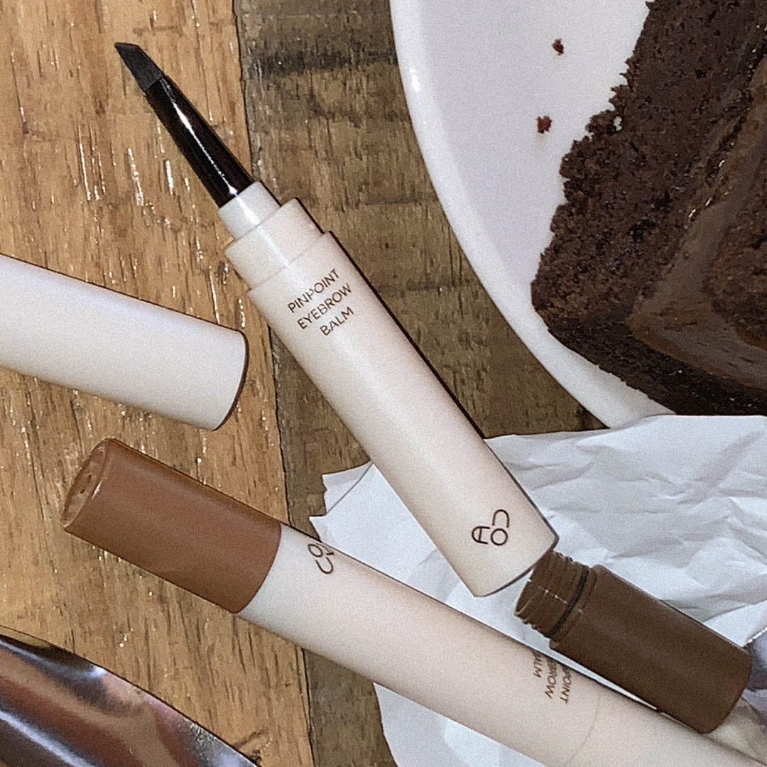 AOU Pinpoint Eyebrow Balm de la marque AOU, stylo maquillage sourcils sur planche en bois, contexte cosmétique.