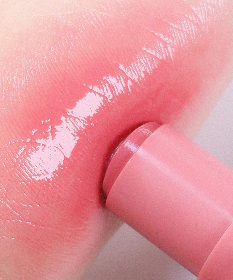 AOU Dewy Bar appliqué sur les lèvres pour un effet hydratant et scintillant, avec un fini rose brillant.