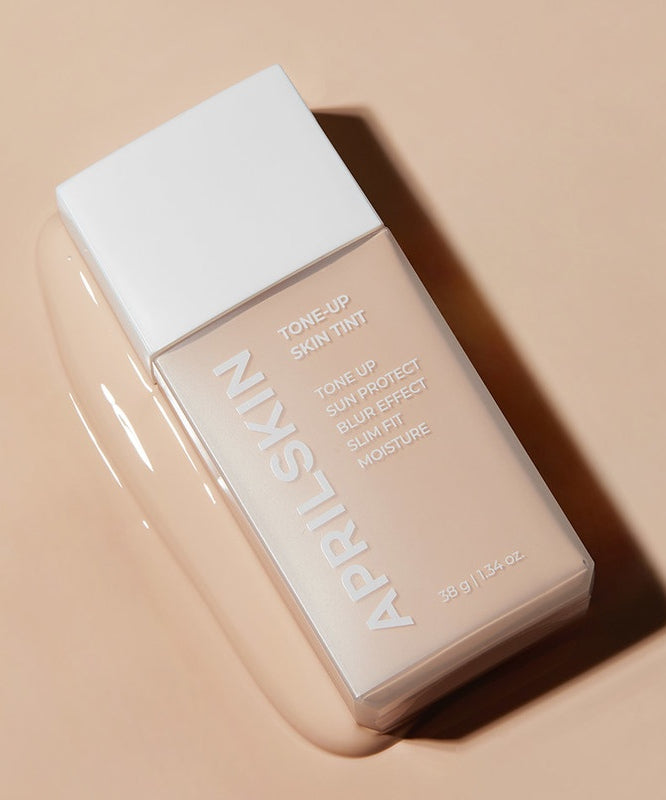 APRILSKIN Tone-Up Skin Tint de APRIL SKIN, flacon maquillage sur fond beige, gros plan produit en lumière naturelle.