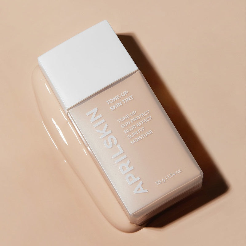 APRILSKIN Tone-Up Skin Tint de APRIL SKIN, flacon maquillage sur fond beige, gros plan produit en lumière naturelle.