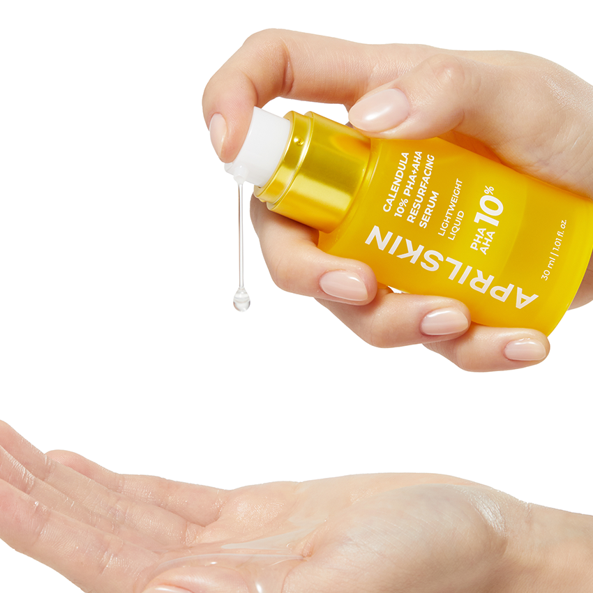 APRILSKIN Calendula 10% PHA+AHA Resurfacing Serum 30ml : main tenant le flacon et appliquant le sérum, fond blanc.