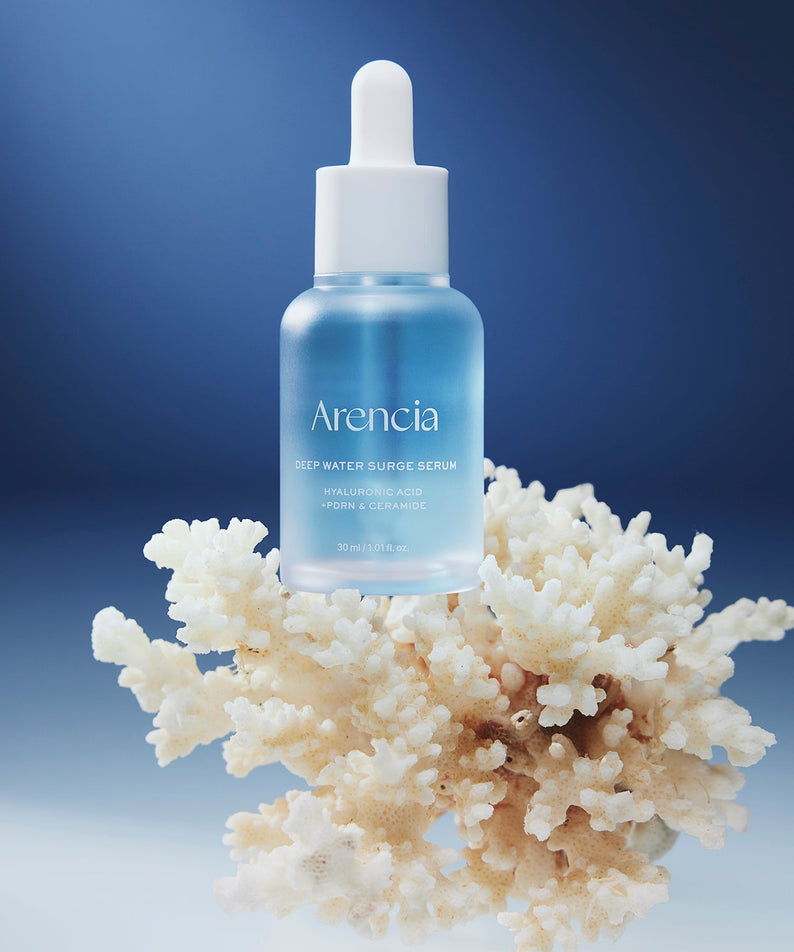 ARENCIA Deep Water Surge Serum 30ml sur fond bleu avec fleurs blanches, bouteille de la marque ARENCIA en gros plan