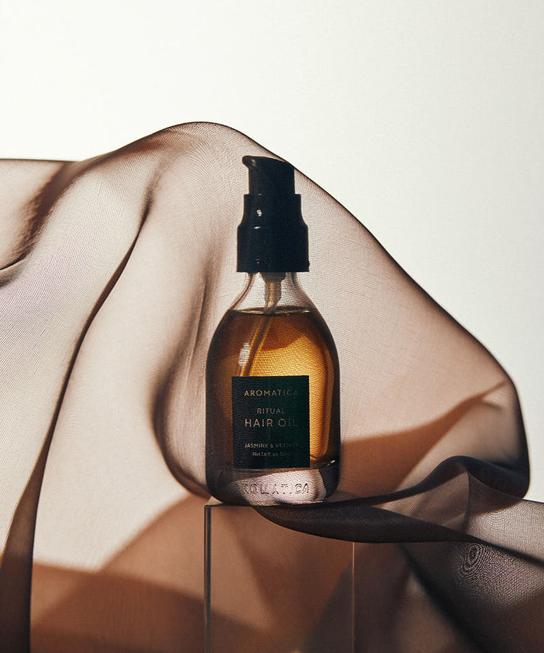AROMATICA Ritual Jasmine & Vetiver Hair Oil 50ml, bouteille sur support, mains et lumière douce, contexte soin cheveux.