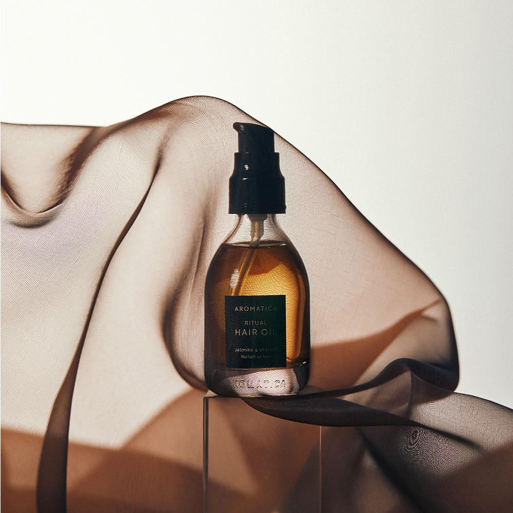 AROMATICA Ritual Jasmine & Vetiver Hair Oil 50ml, bouteille sur support, mains et lumière douce, contexte soin cheveux.
