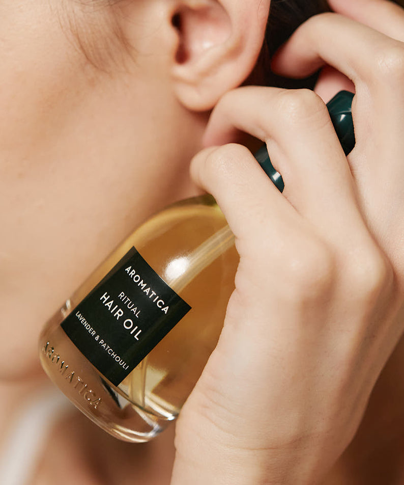 AROMATICA Ritual Lavender & Patchouli Hair Oil 50ml : la main applique l'huile sur cheveux, bouteille AROMATICA, visuel beauté.
