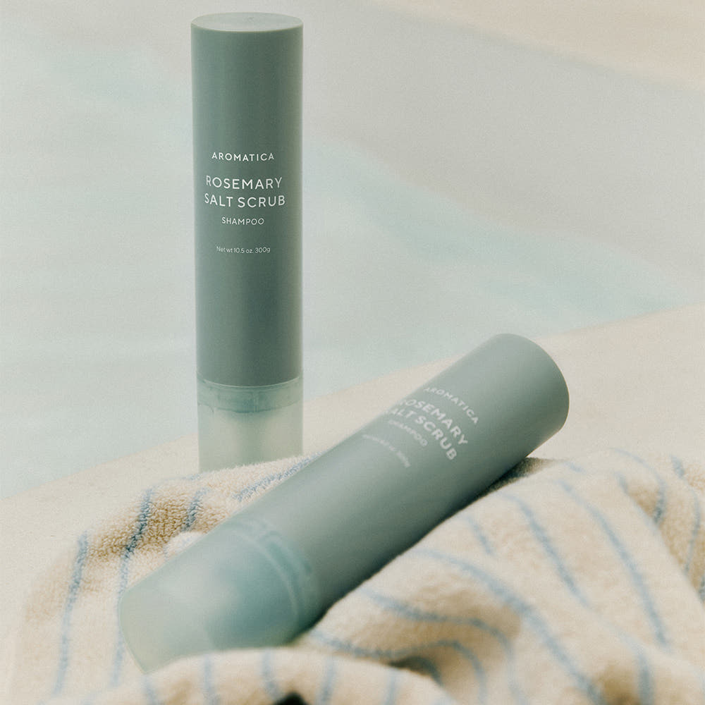 AROMATICA Rosemary Salt Scrub Shampoo de la marque AROMATICA, flacon vert sur serviette, ambiance spa minimaliste.