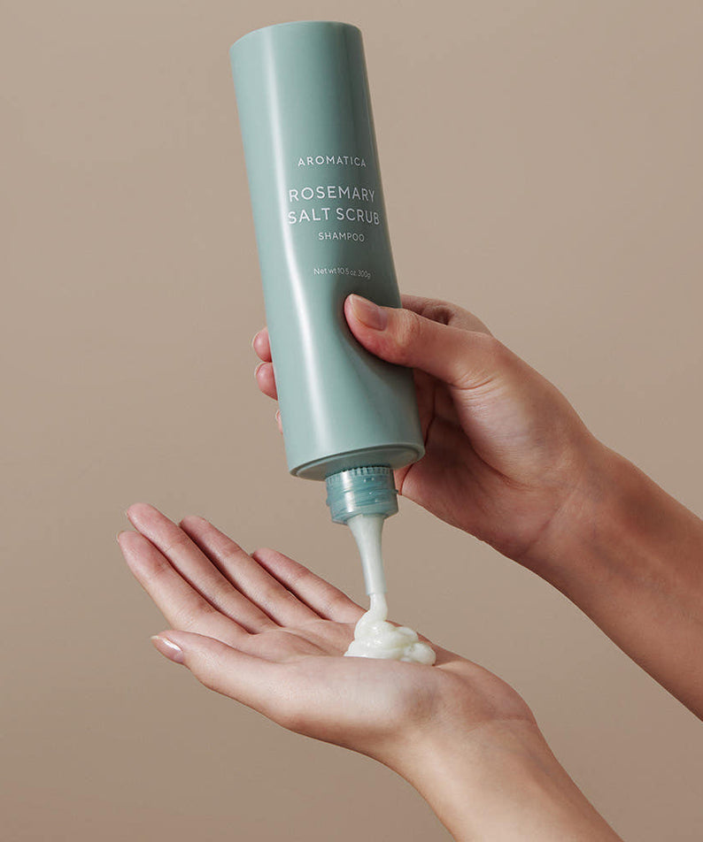 AROMATICA Rosemary Salt Scrub Shampoo, bouteille en main, crème moussante sur les paumes, fond beige minimaliste.