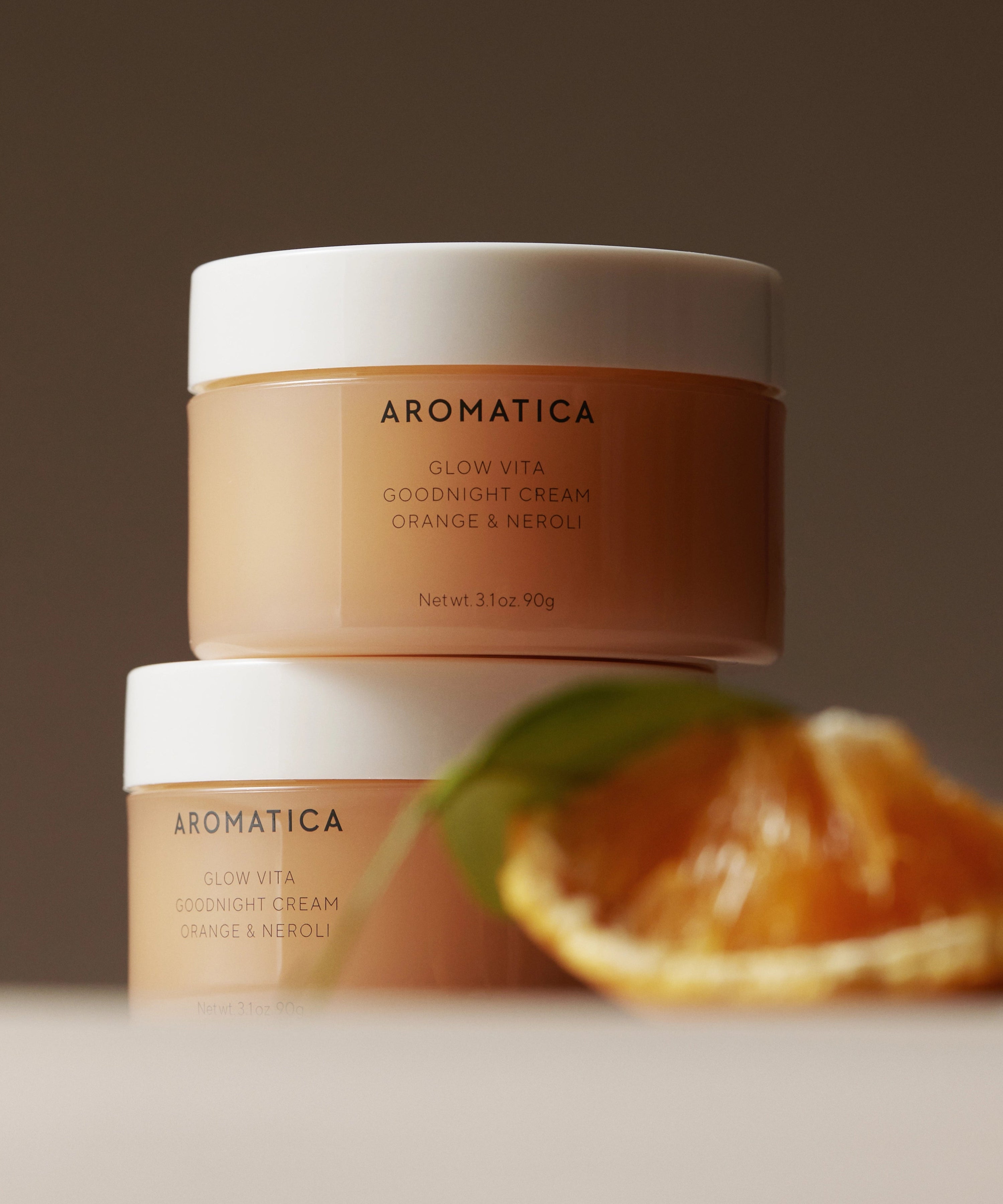 AROMATICA Glow Vita Good Night Cream Orange & Neroli 90G, crème de nuit sur fond brun avec agrume orange en arrière-plan.