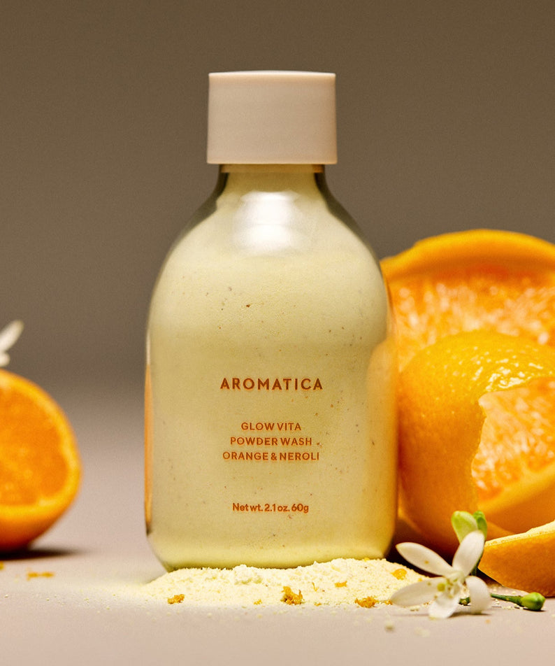 Image du produit AROMATICA Glow Vita Powder Wash Orange & Neroli 60G avec des oranges et fleurs de néroli en arrière-plan.
