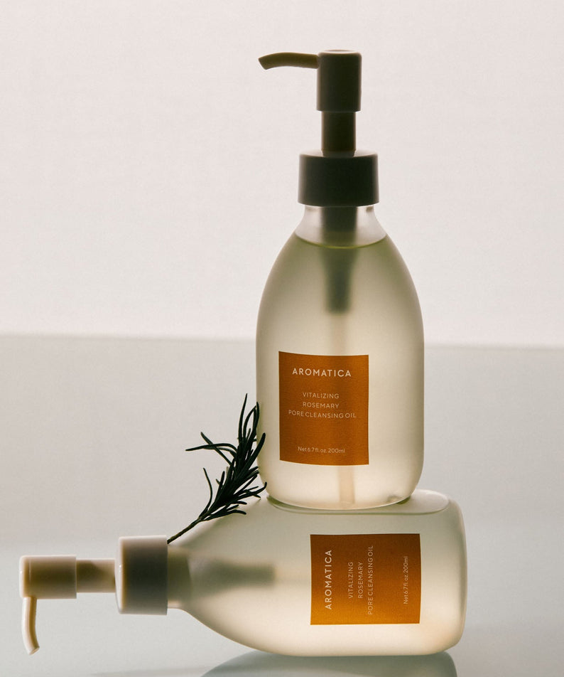 AROMATICA Vitalizing Rosemary Pore Cleansing Oil 200ML, flacons posés élégamment avec branches de romarin en arrière-plan.