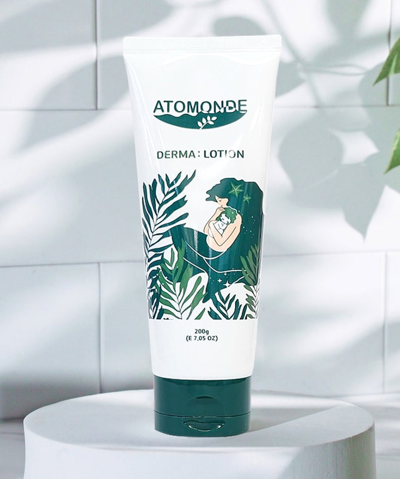 ATOMANDE Baby Derma Infant Lotion 200g, tube sur un socle, décor salle de bain blanche avec feuilles vertes.