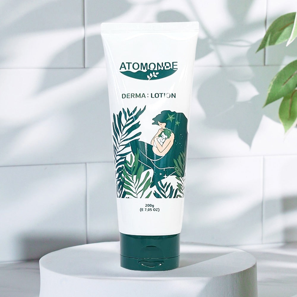 ATOMANDE Baby Derma Infant Lotion 200g, tube sur un socle, décor salle de bain blanche avec feuilles vertes.