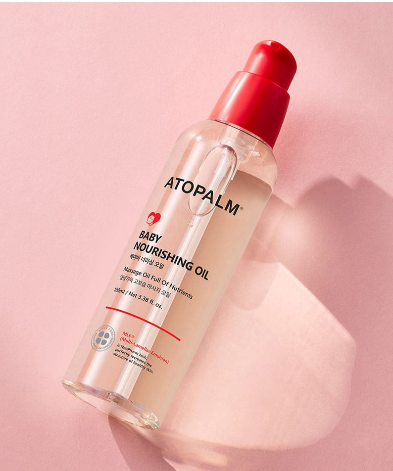 Bouteille de ATOPALM Baby Nourishing Oil 100ml sur fond rose.