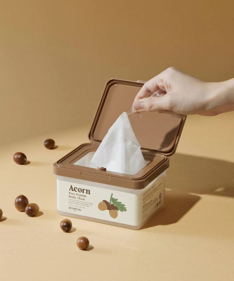 SKINFOOD Acorn Pore Peptide Daily Mask 30p 270g, boîte ouverte sur fond beige, main retire un tissu masque, contexte visuel spa.