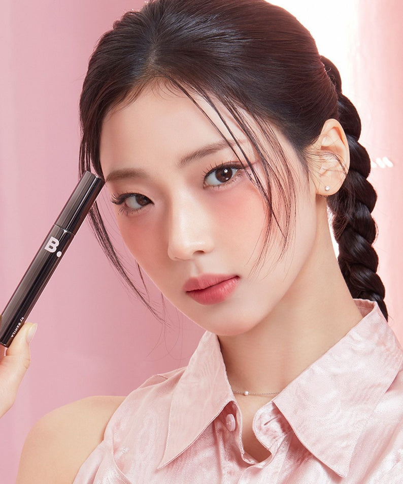 BANILA CO Powerproof Mascara de BANILACO : maquillage des yeux, mascara tenu près du visage sur fond rose.