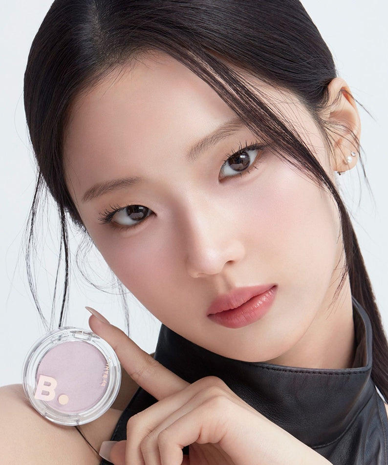 Décris l'image en français : BANILA CO Silky Glow Highlighter, jeune femme maquillée, pot rose sur fond clair, éclat lumineux.