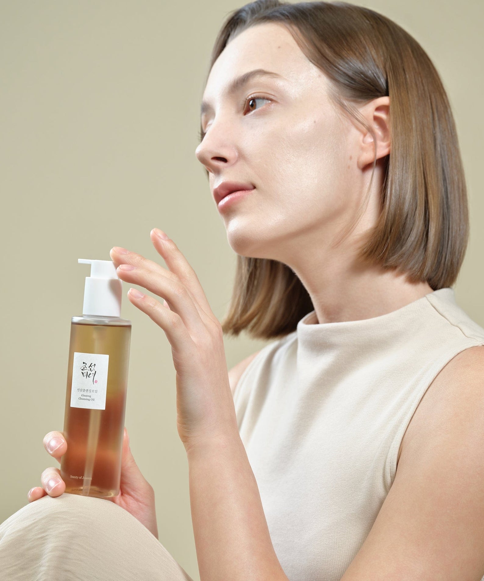 BEAUTY OF JOSEON Ginseng Cleansing Oil 210ml, femme appliquant l’huile nettoyante de la marque dans un décor studio beige