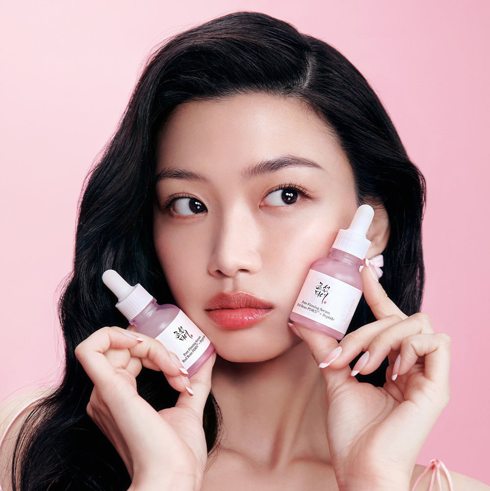 Décris l'image en français en mentionnant le produit, la marque et le contexte visuel : BEAUTY O JOSEON Red Bean PDRN Pore Firming Serum 30mL, flacons tenus par une femme sur fond rose.