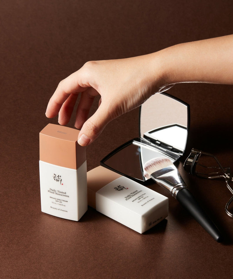 BEAUTY OF JOSEON Daily Tinted Fluid Sunscreen 50ml, pack sur fond brun, main appliquant un fluide teinté, marque visible.