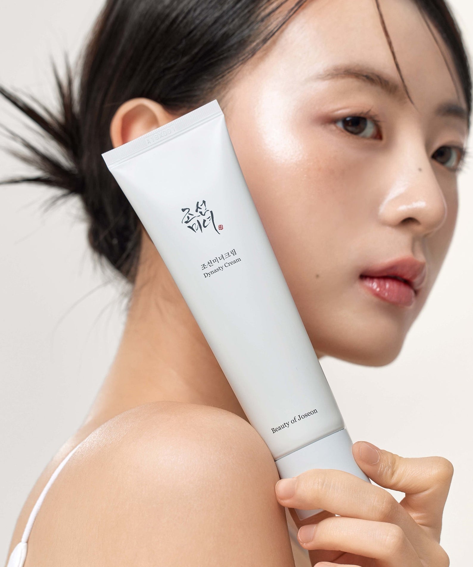 BEAUTY OF JOSEON Dynasty Cream 100ml, tube blanc sur peau, portrait beauté fond clair, marque et produit en évidence