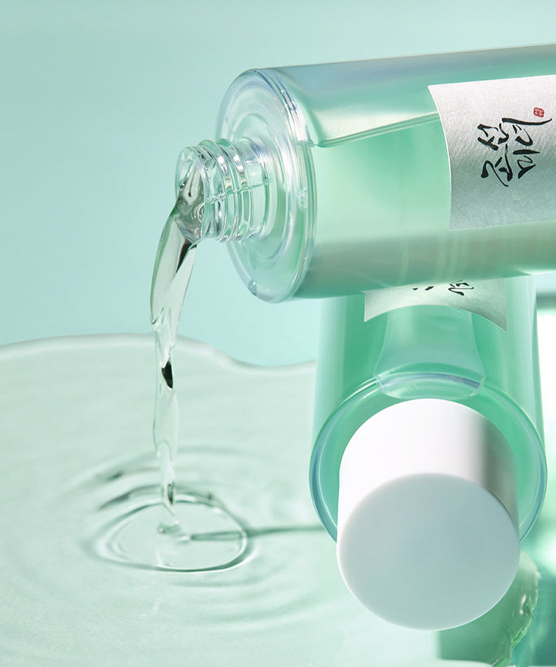 BEAUTY OF JOSEON Green Plum Refreshing Toner AHA + BHA 150ml versé sur une surface, flacon esthétique et transparent en arrière-plan.