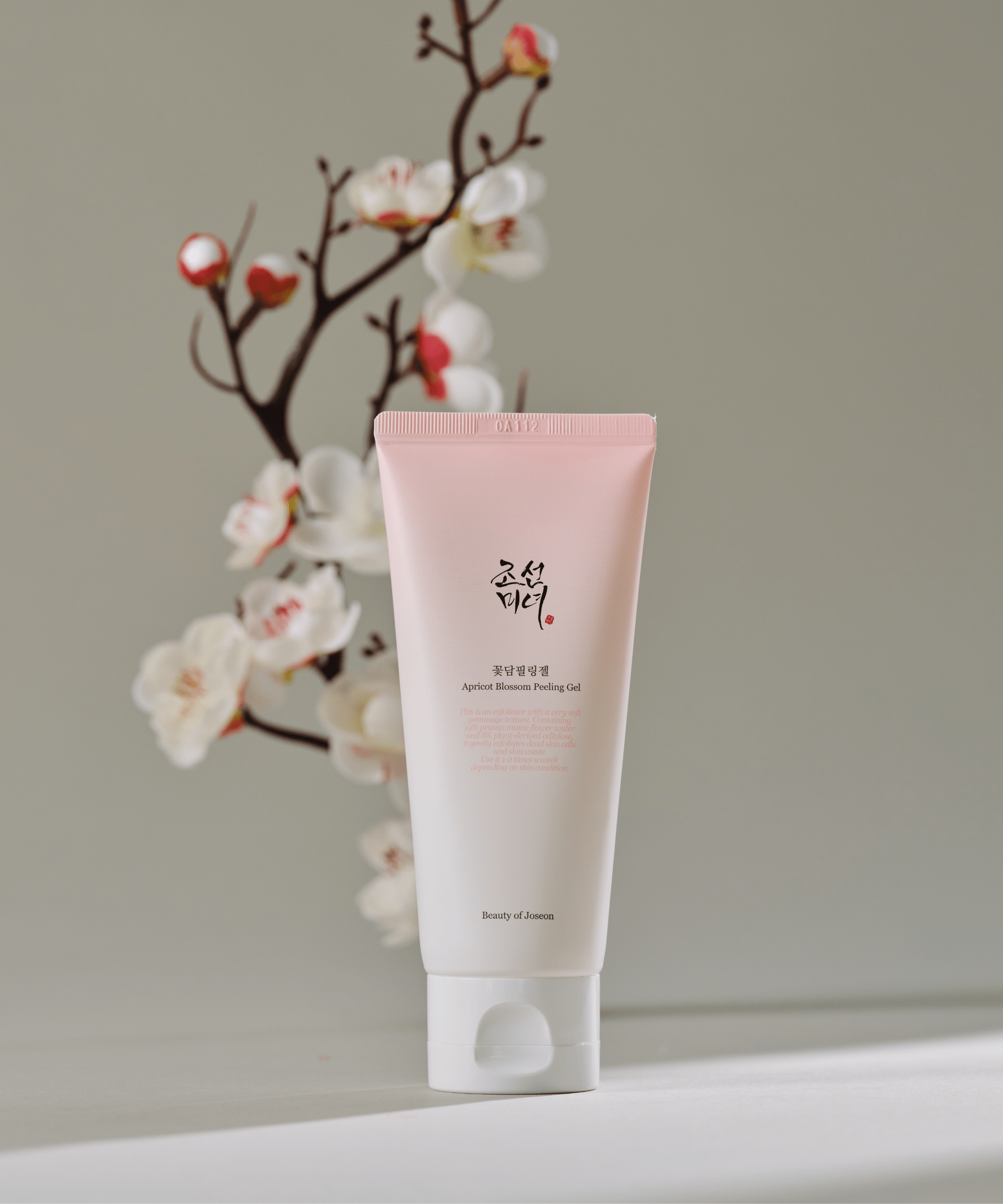 BEAUTY OF JOSEON Apricot Blossom Peeling Gel 100ml, tube rose sur fond clair, fleurs d’abricot en arrière-plan