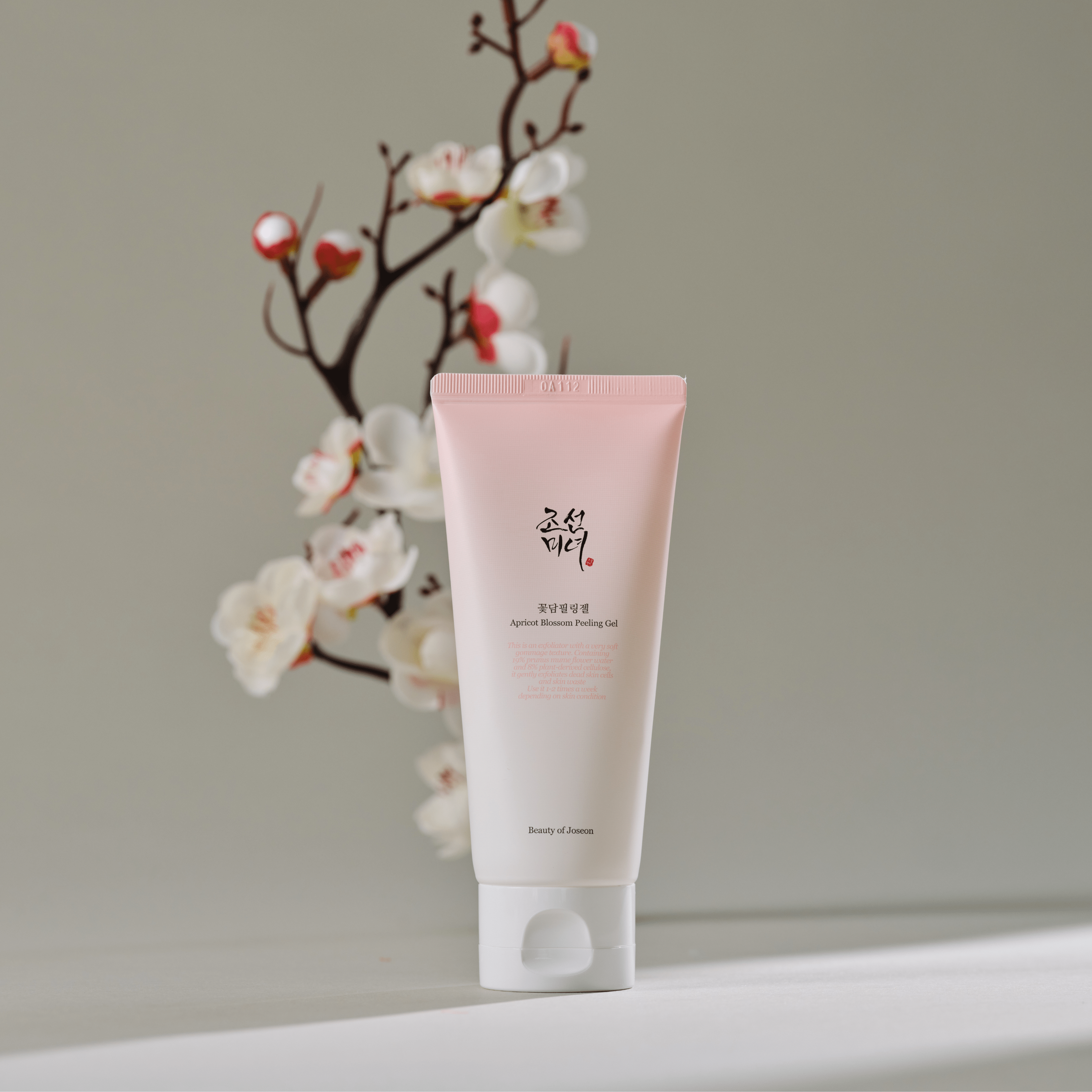 BEAUTY OF JOSEON Apricot Blossom Peeling Gel 100ml, tube rose sur fond clair, fleurs d’abricot en arrière-plan