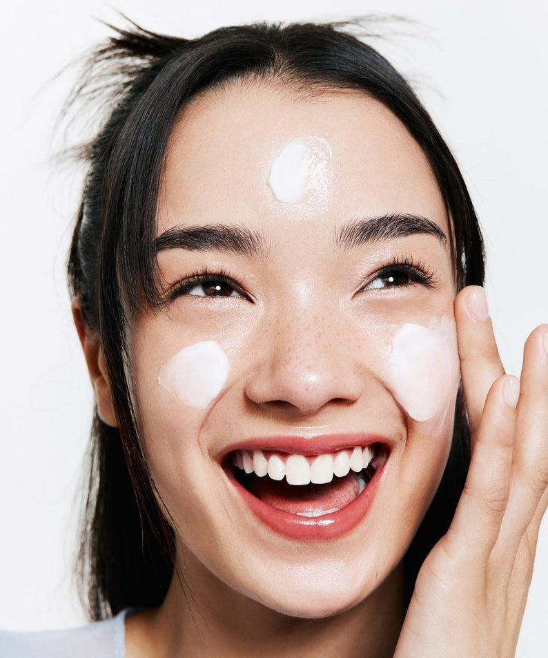 Femme souriante appliquant BELIF The True Cream Moisturizing Bomb 50ml sur son visage.