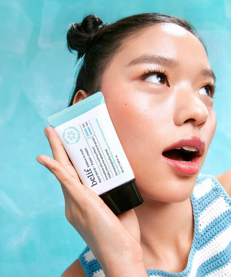 Femme tenant BELIF Aqua Bomb Frozen Cream 50ml avec fond bleu, hydratation intense pour la peau. Produit phare de BELIF.