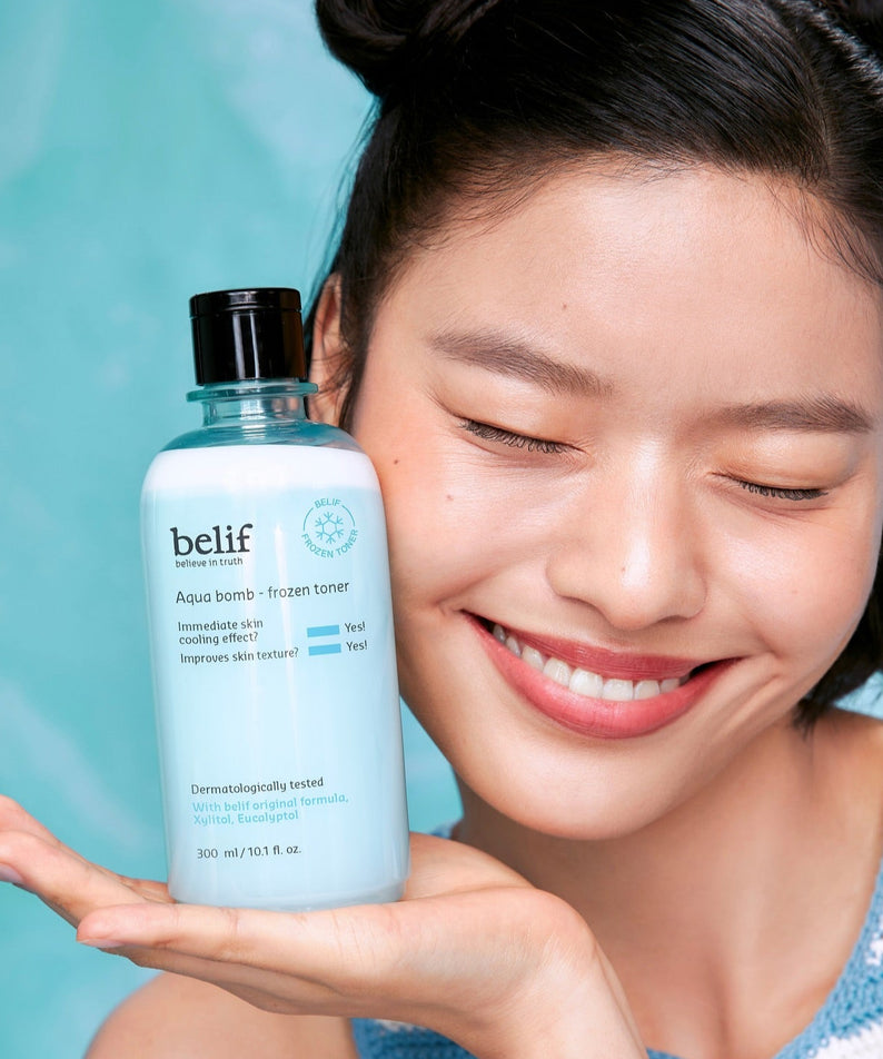 Femme souriante tenant une bouteille de BELIF Aqua Bomb Frozen Toner 330ml, toner rafraîchissant pour une peau éclatante.