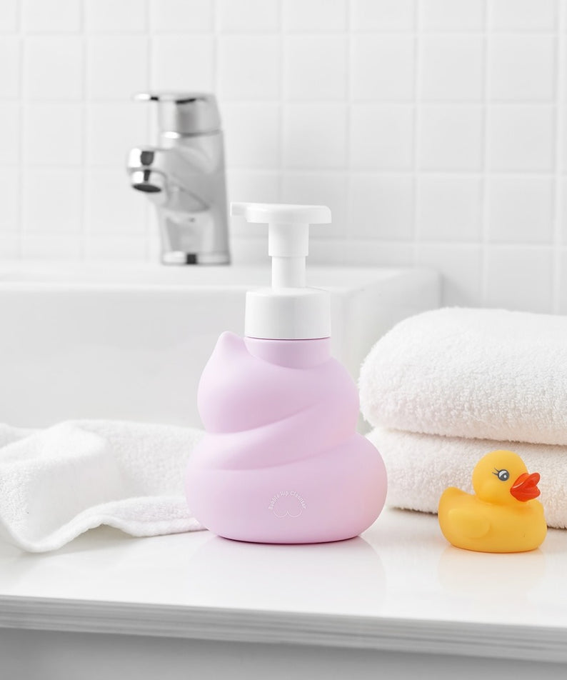 Décris l'image en français : BELLBOY STUDIO Hippong Bubble Butt Cleanser en flacon rose sur serviettes, salle de bain.