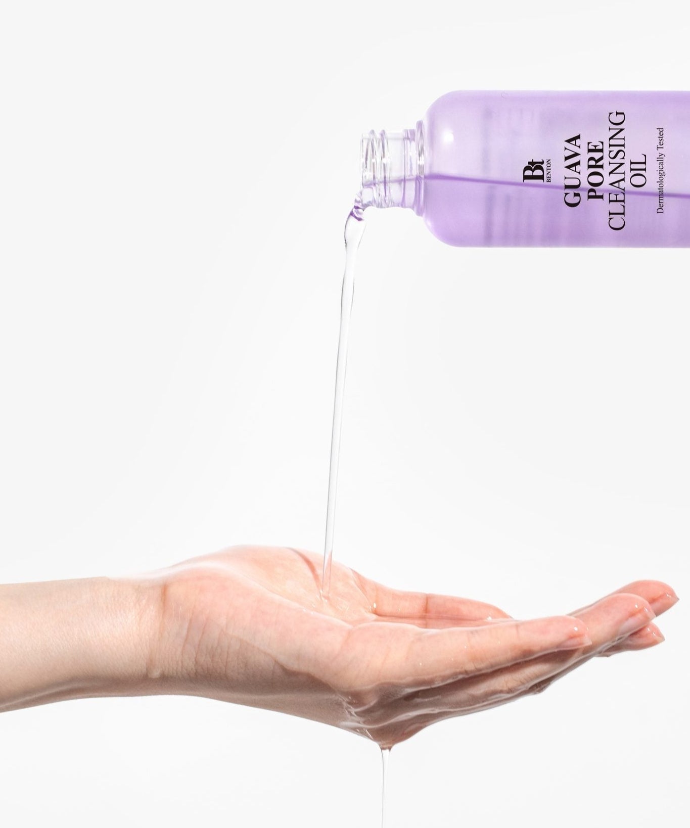 BENTON Guava Blackhead Pore Cleansing Oil 200ml en train d'être versé dans une main ouverte pour montrer sa texture et sa clarté.