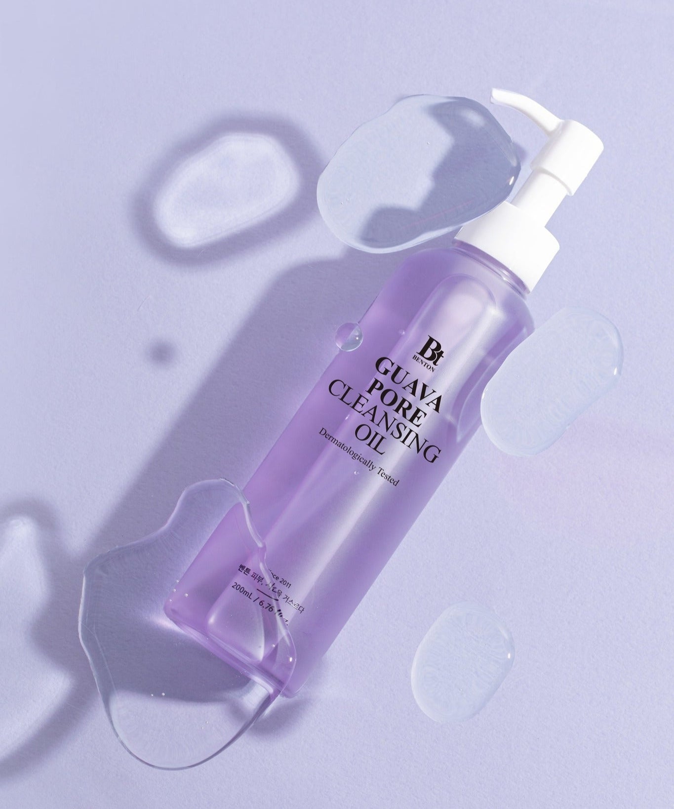 BENTON Guava Blackhead Pore Cleansing Oil 200ml sur fond violet avec gouttes d'huile, produit de soin de la peau.