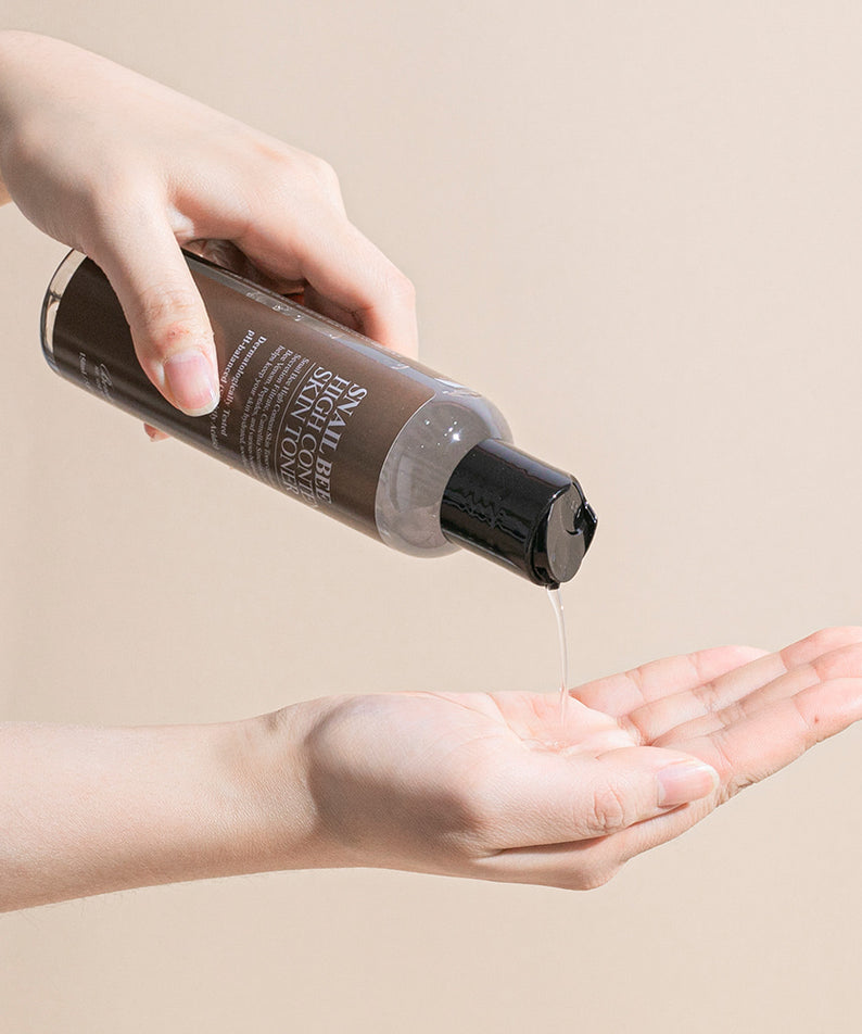 Décrivez l'image en français : BENTON Snail Bee High Content Skin Toner 150ml, produit cosmétique sur main, texture versée.