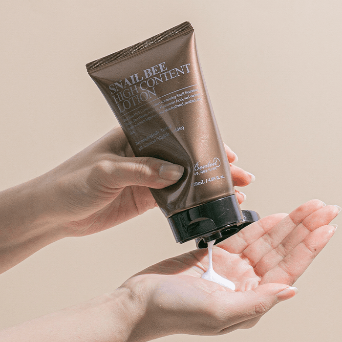 Main tenant BENTON Snail Bee High Content Lotion 120ml, crème s’écoulant sur la main, fond beige, image produit