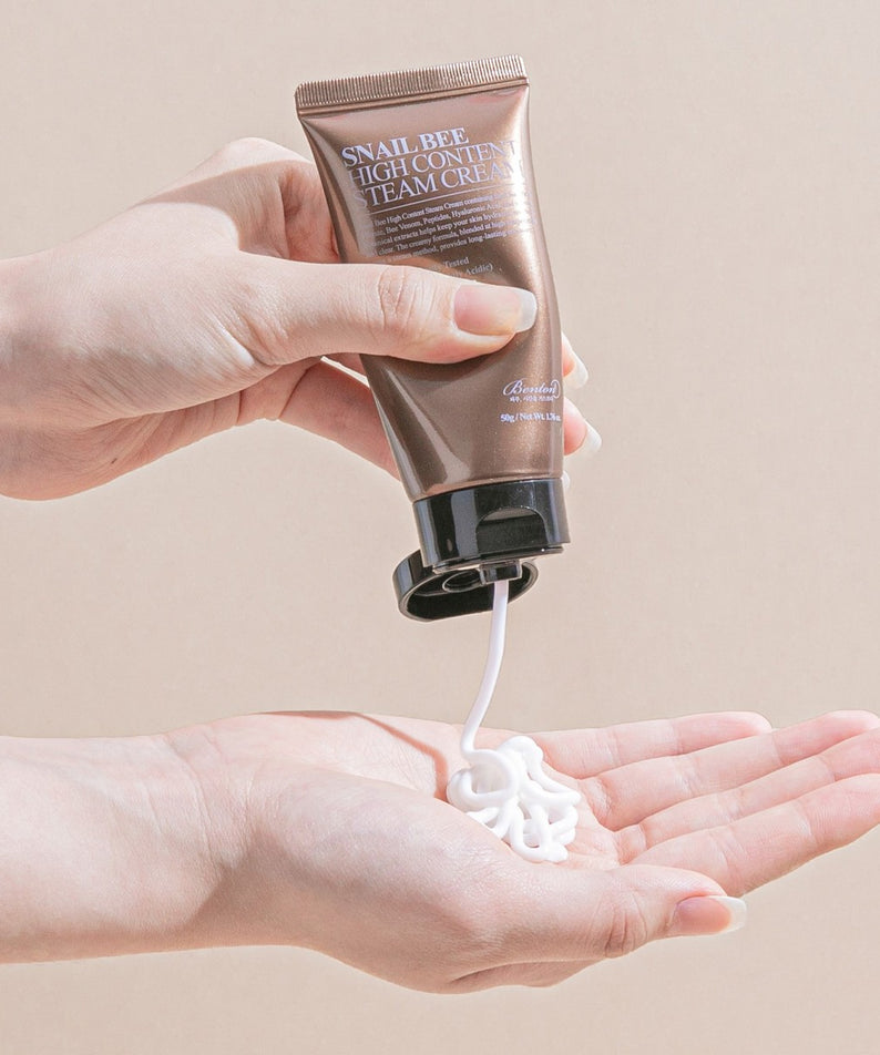 Main tenant le BENTON Snail Bee High Content Steam Cream 50g, marque BENTON, crème sur la main, fond clair