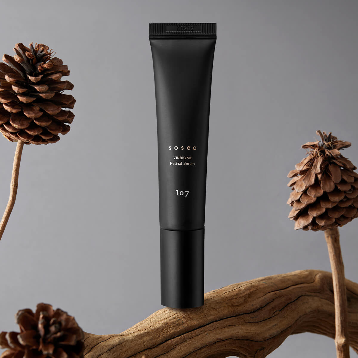 107 Soseo Vinbiome Retinal Serum 20ml : tube noir sur fond gris, décor pommes de pin et bois, lumière studio.