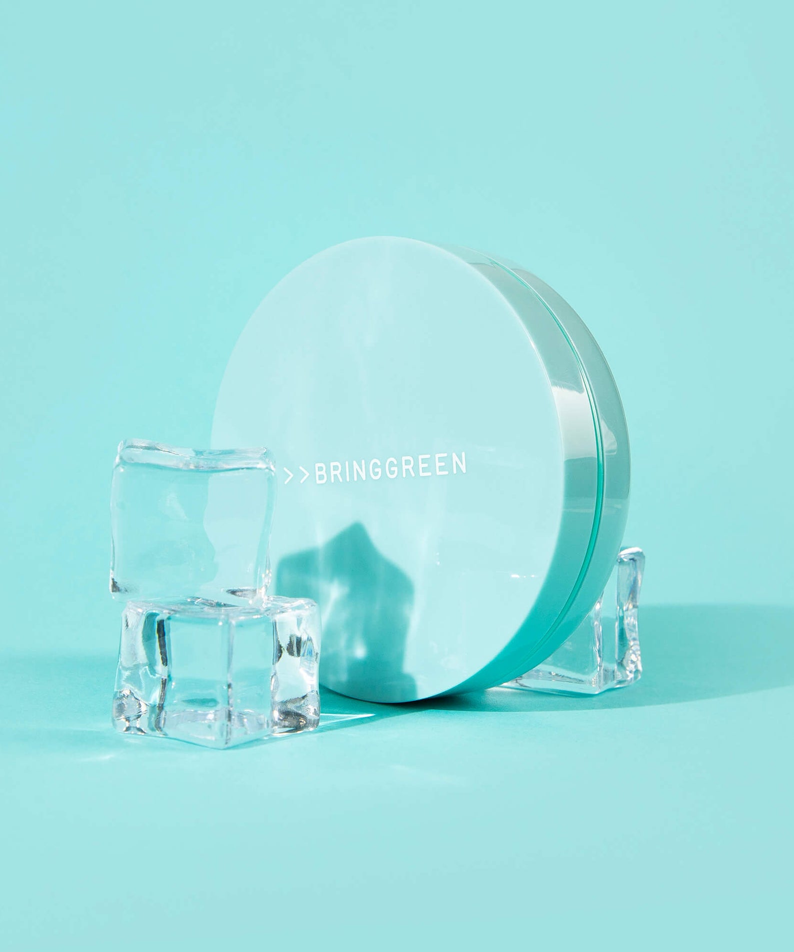 BRINGGREEN Tea Tree Cica Tone Up Sun Cushion de la marque BRINGGREEN sur fond turquoise, boîte et cubes de glace.