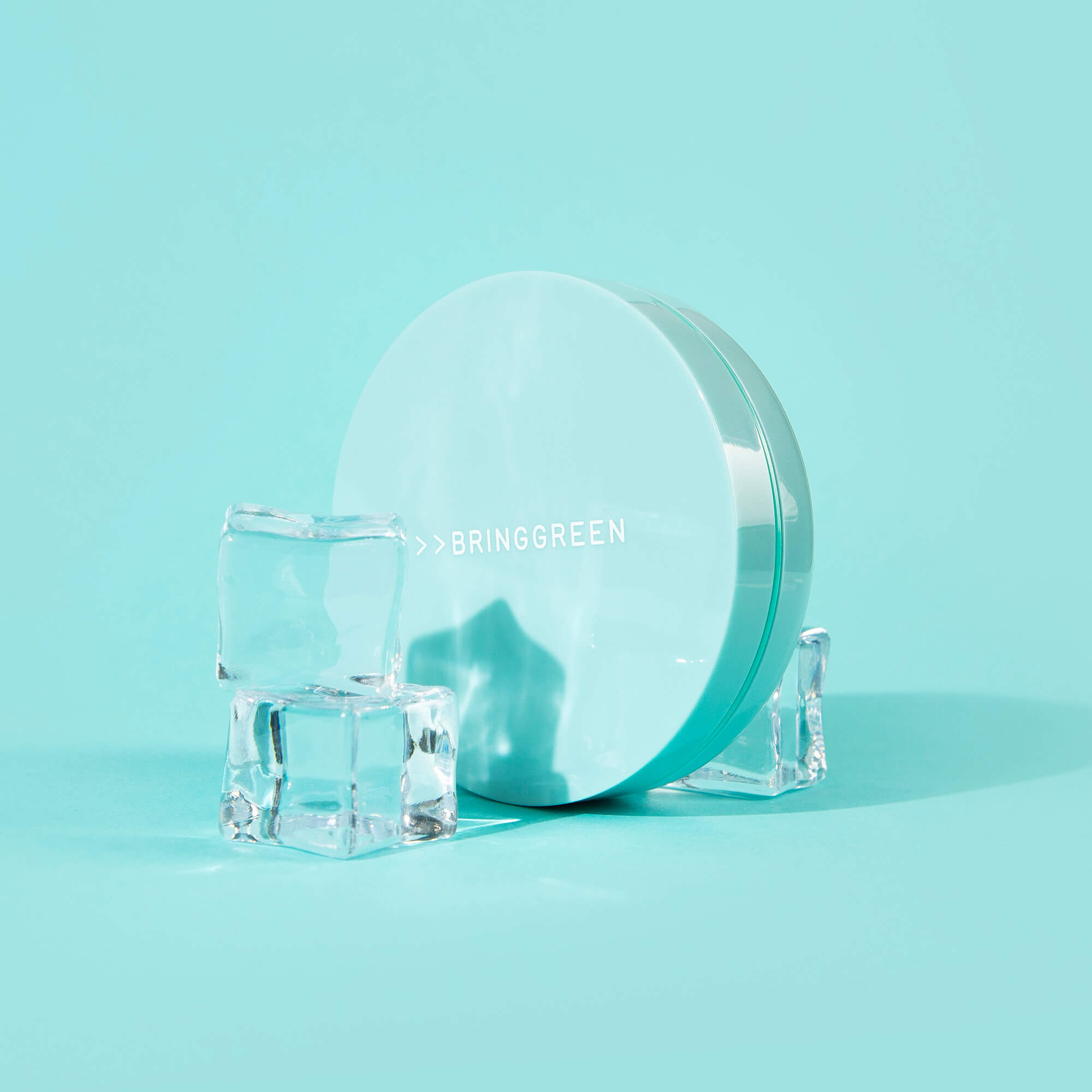 BRINGGREEN Tea Tree Cica Tone Up Sun Cushion de la marque BRINGGREEN sur fond turquoise, boîte et cubes de glace.