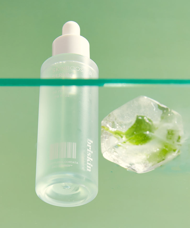 Sérum BRISKIN Houttuynia Cordata Exo-Barrier Skinbooster 50ml sur fond vert, bouteille élégante à côté d'un glaçon avec plante verte.