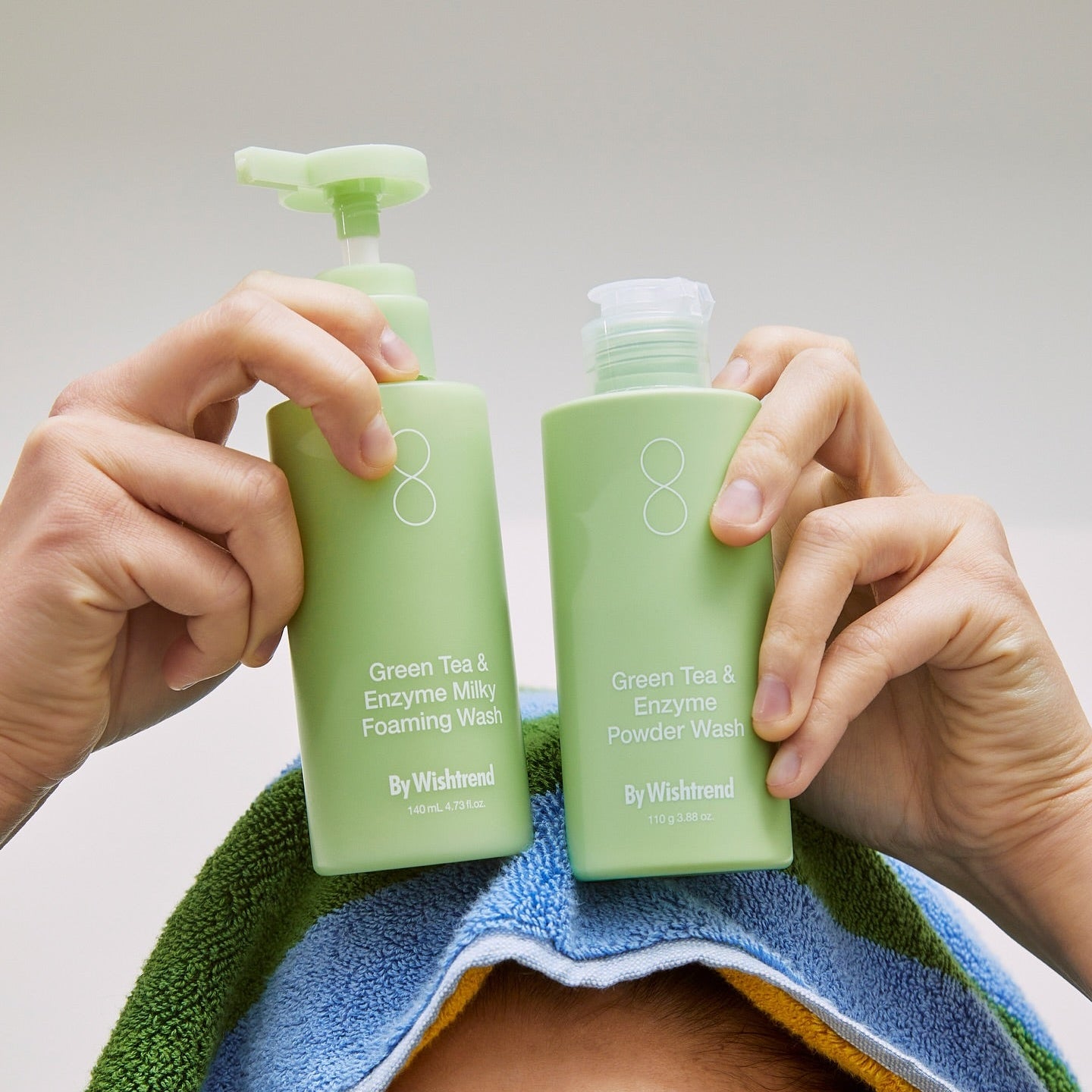 BY WISHTREND Green Tea & Enzyme Powder Wash 110g, mains tenant le produit sur serviette, contexte soin visage.
