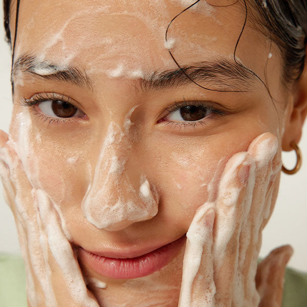 BY WISHTREND Green Tea & Enzyme Milky Foaming Wash 140ml : femme mousse nettoyante sur visage, gros plan lumineux.