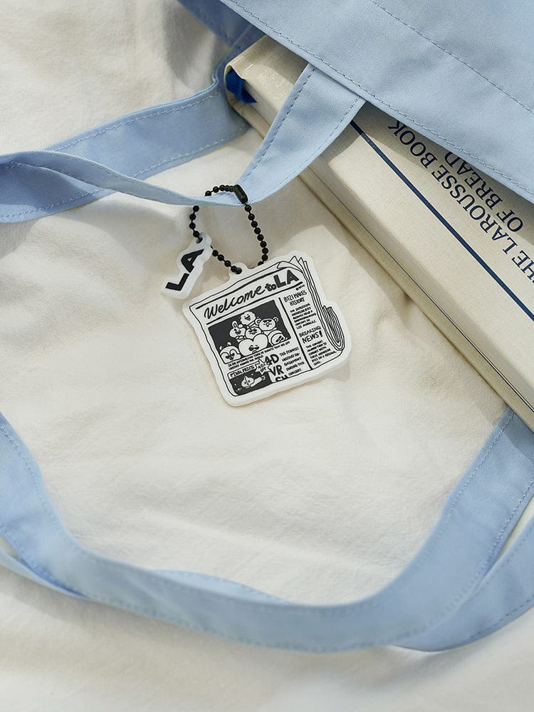 BT21 ACRYLIC KEYRING LA CITY EDITION, porte-clés acrylique officiel BT21 sur sac en tissu bleu, fond clair.