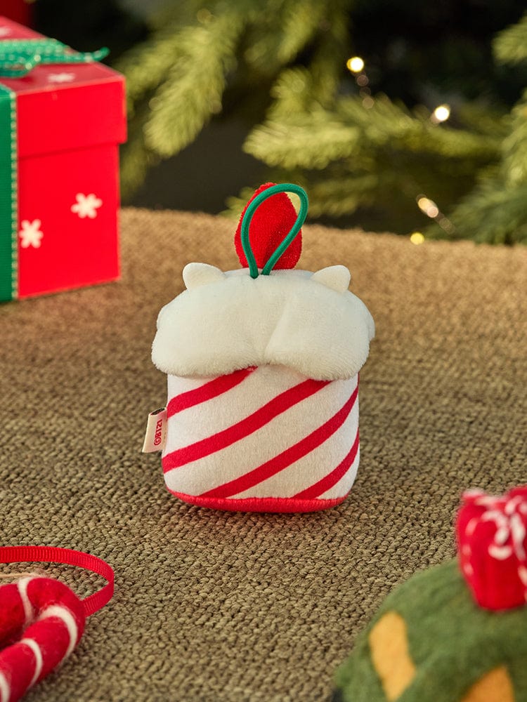 BT21 RJ mini minini ORNAMENT PLUSH KEYRING PETITE HOLIDAY : porte-clés peluche RJ sur table de Noël, sapin et cadeaux en arrière-plan.