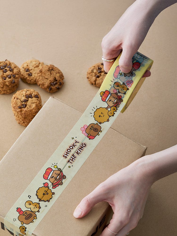 BT21 SHOOKY THE KING PACKING TAPE LINE FRIENDS, ruban décoratif posé sur carton, mains en train de sceller des colis.