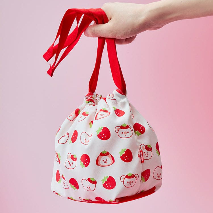 Main tenant le BT21  Strawberry Party String Pouch de la marque BT21, petit pouch blanc motif fraises, fond rose.